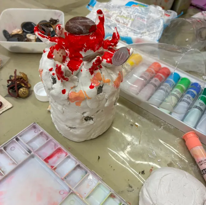 机の上に置かれた絵具と、粘土の創作物